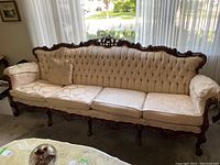 Full front view of vintage French provincial style couch showing button tufting, carved wooden frame, and three seat cushions.