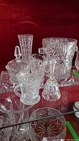 Photo showing various pieces of the crystal glassware set including ice bucket, covered sugar bowl, creamer, bud vase, and small containers with lids on a glass shelf with red background.