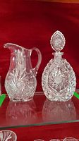 Both crystal decanter and pitcher shown together on red background, highlighting their shapes and cut patterns.
