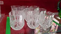 Group of nine clear crystal rock glasses with detailed cut patterns on a reflective surface.