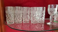 Six crystal highball glasses in a row with the wine goblet visible to the side, showing the cut glass design pattern and thick bottoms.