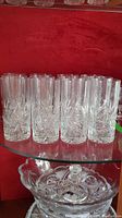 Full front view of twelve pinwheel cut crystal glasses arranged in rows on a glass shelf against a red background.