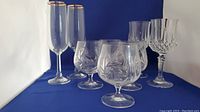 Eight crystal glasses on blue background showing four pinwheel pattern glasses, two wine, two champagne flutes.
