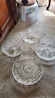 Four clear crystal serving pieces displayed on carpet: one divided serving tray on pedestal and three bowls with distinctive cut glass patterns.