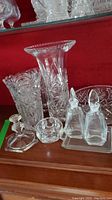 Crystal vases including tall, medium and small sizes with etched floral or geometric designs, accompanied by small round crystal items and a stopper.
