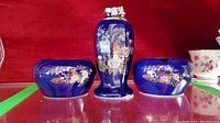 Tabletop lighter and two porcelain ashtrays set, cobalt blue with hand-painted floral and bird designs on shelf with red background