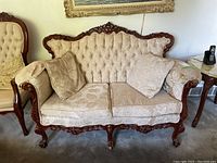 Full front view of vintage French provincial love seat showing carved wood frame, tufted backrest, beige floral damask upholstery, and two cushions.