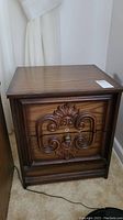 Front view of wooden night table with carved drawer front and laminate top showing wear and scratches.