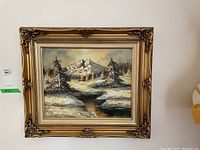 Full front view of the framed oil painting showing mountain and snowy trees with water reflecting the scene, hung on a white wall.
