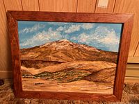 Full view of the framed landscape painting showing mountains, blue sky, and vegetation.