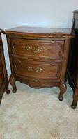 Front view of vintage wood side table with two drawers, brass handles, and carved leg details