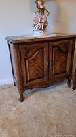 Front view of side table showing two cabinet doors and carved details on doors and base