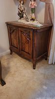 Front view of a vintage wooden side table with storage cabinet, carved detailing, and decorative accents on top.