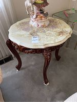 Overall view of round scalloped-edge marble top and carved wood base with decorative apron and cabriole legs