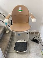 Front view of stairlift seat assembly on tiled landing showing seat, armrests and footrest