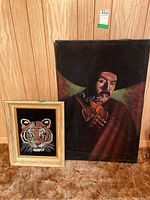 Both velvet paintings leaning against a wood wall, showing the framed tiger image and the larger unframed male portrait.
