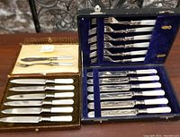 Two boxed sets of antique silver plated cutting utensils and forks displayed together showing the knives with mother of pearl handles and ornate forks in blue velvet lining.