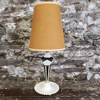 Front view of art deco table lamp showing geometric black and white stem, hobnail milk glass base, and burlap shade on rustic wood surface