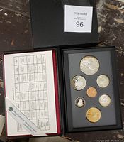 Top view of the black box with 7 commemorative coins and the accompanying specification insert detailing composition and measurements, as well as the Royal Canadian Mint branded ribbon.