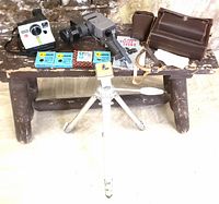 Full lot showing Canon movie camera with attached lens, leather carrying case, Polaroid OneStep Land Camera, Eaton's collapsible tripod, Canon lens filters, and manuals arranged on rustic wooden bench.