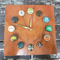 Front view of the square wooden wall clock with twelve colorful Canadian beer bottle caps marking the hours, gold hour and minute hands and a red second hand, set against a wood background.