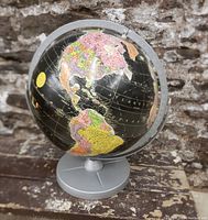 Photo of mid-century black world globe showing North and South America with vibrant colored countries mounted in a silver metal base.