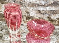 Photo showing the cranberry art glass vase and dish with a brick background. Vase has candy cane white swirl and heavy clear base. Dish has wavy rim and bubbles in glass.