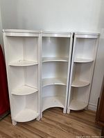 Set of three white painted wood corner shelves, showing front view and multiple shelves per unit.