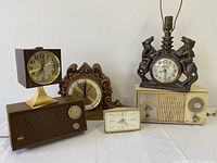 Five items including three clocks and two clock radios on white surface, front view