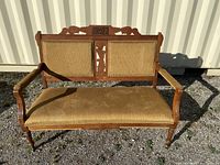 Front view of antique wooden settee showing carved wooden frame and upholstered seat and back cushions in tan ribbed fabric.