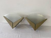 Pair of triangular Art Deco Revival style wall sconces with textured metal bases and ribbed removable glass shades placed on white surface against wall.