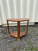 Front view of the Art Deco style solid wood side table showing the scalloped top and lower shelf connected by three fluted legs with curved feet.