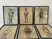 Six framed prints showing Canadian soldiers in historical uniforms, arranged on a surface and hung on a wall.