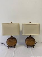 Front view showing both lamps with their cream rectangular shades and hammered gold-finished oval bases on footed stands.