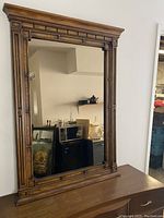 Full front view of the wood framed mirror positioned on tabletop, showing detailed frame, large reflective tinted glass and its proportions.