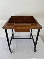 Front view showing the wood top with built-in divided compartments and black metal legs with caster wheels