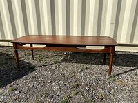 Full side-angle view of wooden coffee table showing four tapered legs and brass leg caps, table base with open cut-out design beneath the tabletop.