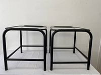 Pair of black metal frame side tables with rectangular clear glass tops, photographed from front angle showing their shape and condition.