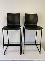 Front view of the pair of black stackable stools with plastic seats and metal sled bases.