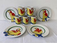 Front view showing 5 mugs and 4 plates arranged with parrot and ring design visible on all dishes.