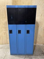 Front view of the 3-door lockers showing blue lower doors and black upper panels with recessed handles.