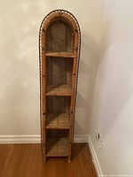 Front view of tall, narrow rattan shelf unit showing its arched top and four shelves.