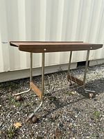 Side angled view of the vintage wood and metal record stand showing wooden top with metal legs on casters and metal record rack below.