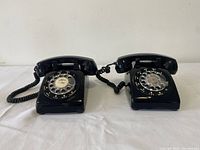 Set of 2 black rotary dial telephones shown side by side on white surface.
