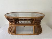 Front angle view showing the oval shape, bamboo frame, glass top, and slatted bamboo shelf.