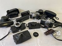 Wide shot of all cameras and accessories laid out showing various vintage cameras and camera cases, flash unit with reflector, and lens cap.