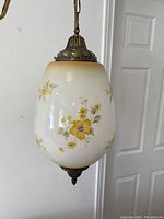 Front angled view showing the floral painted yellow flowers on frosted white glass shade, brass fixture details at top and bottom, and chain for hanging.