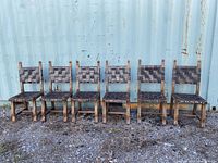 Front view of the six wood dining chairs with woven dark brown leather straps, showing full chair frames and wear on leather and wood.