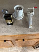 Three antique kitchen gadgets on countertop: BOKAR coffee tin, mouli grater, and white food mill.