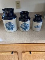 Three McCoy ceramic planters arranged by size on kitchen counter, showing blue and white color with fruit motifs.
